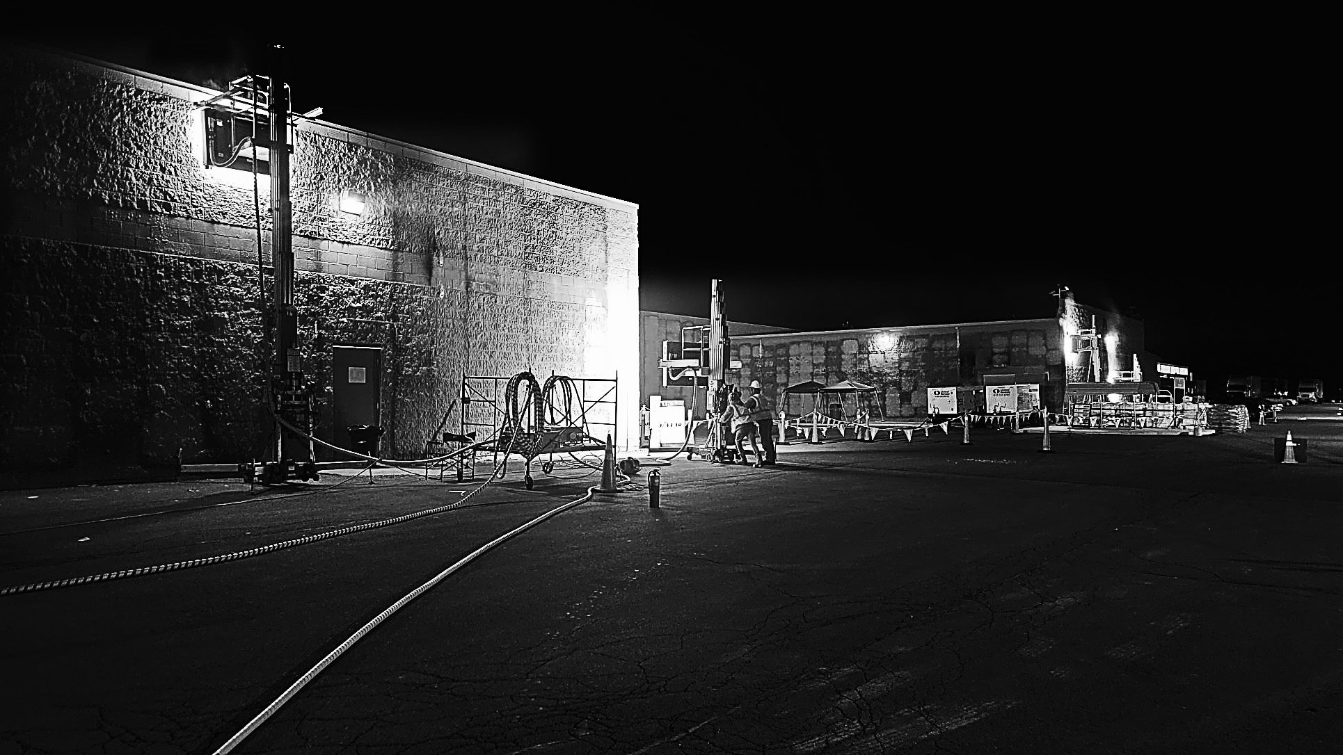 Crews clearing coating from a masonry wall at night, the wall glowing under directed thermal energy